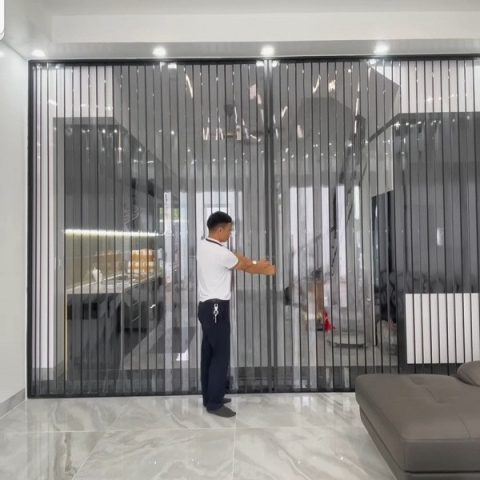 Cửa xếp lá nhựa PVC màu trắng xám, mở ra không gian phòng khách hiện đại có điều hòa.
