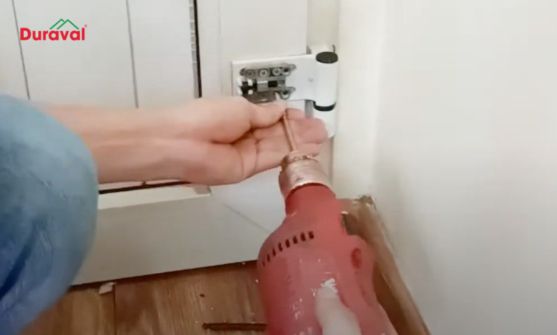 Tháo các vít cố định bản lề cửa nhựa lõi thép bằng tua vít điện