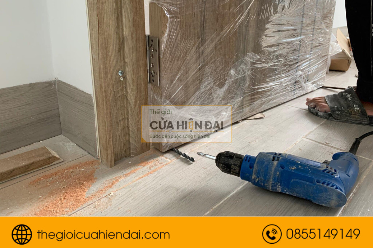 Thợ đang cố định bản lề chắc chắn lên cánh cửa nhựa composite.