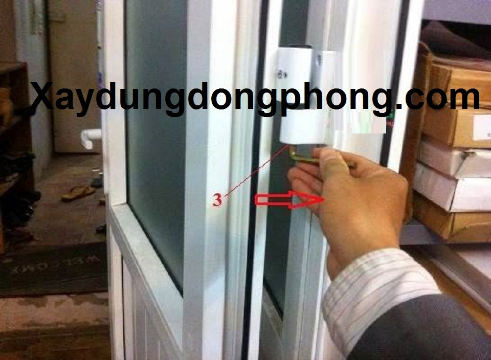 Thợ đang điều chỉnh vít nâng cánh cửa nhựa tại bản lề 3D để sửa cửa bị xệ và lệch.